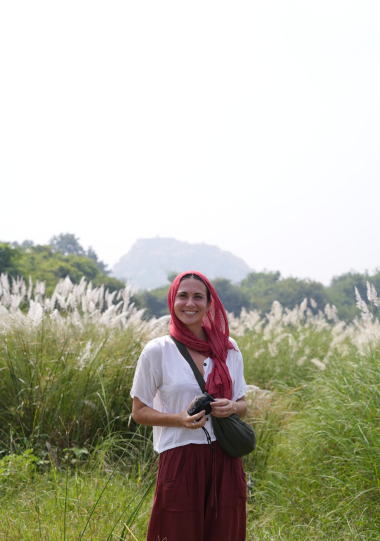 Profesora de yoga sonriendo en un entorno natural con flores blancas y pañuelo rojo, representando retiros de yoga