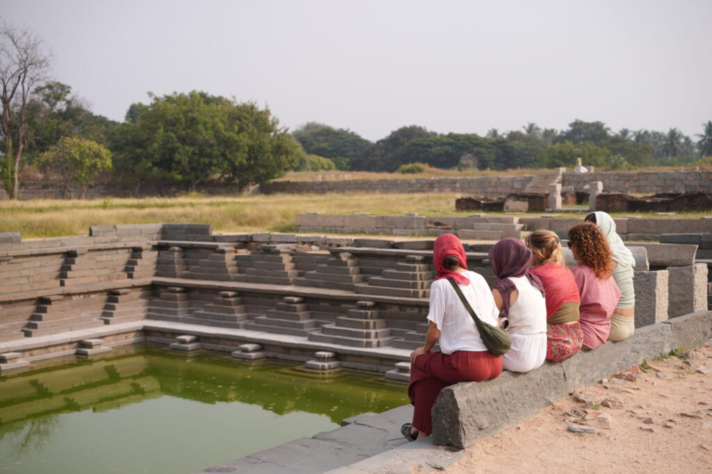 Personas sentadas junto a una pushkarani, antiguo tanque de agua en Hampi