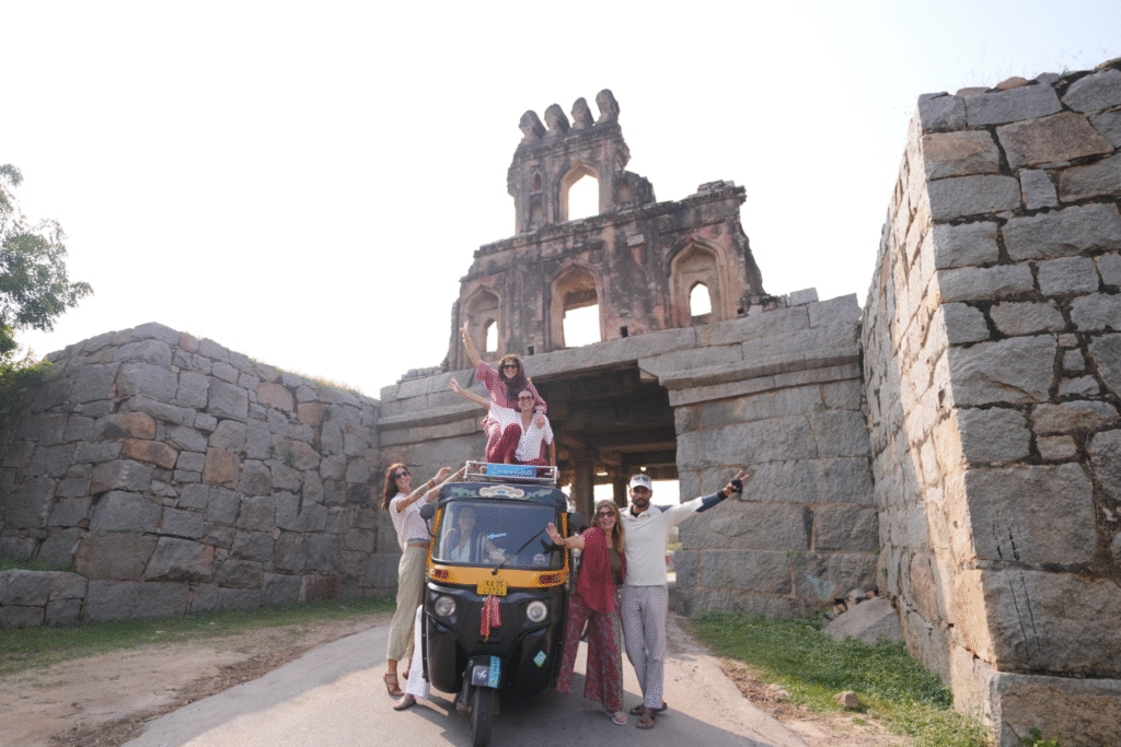 Grupo del retiro de yoga en Hampi posando sobre un auto rickshaw frente a templos antiguos